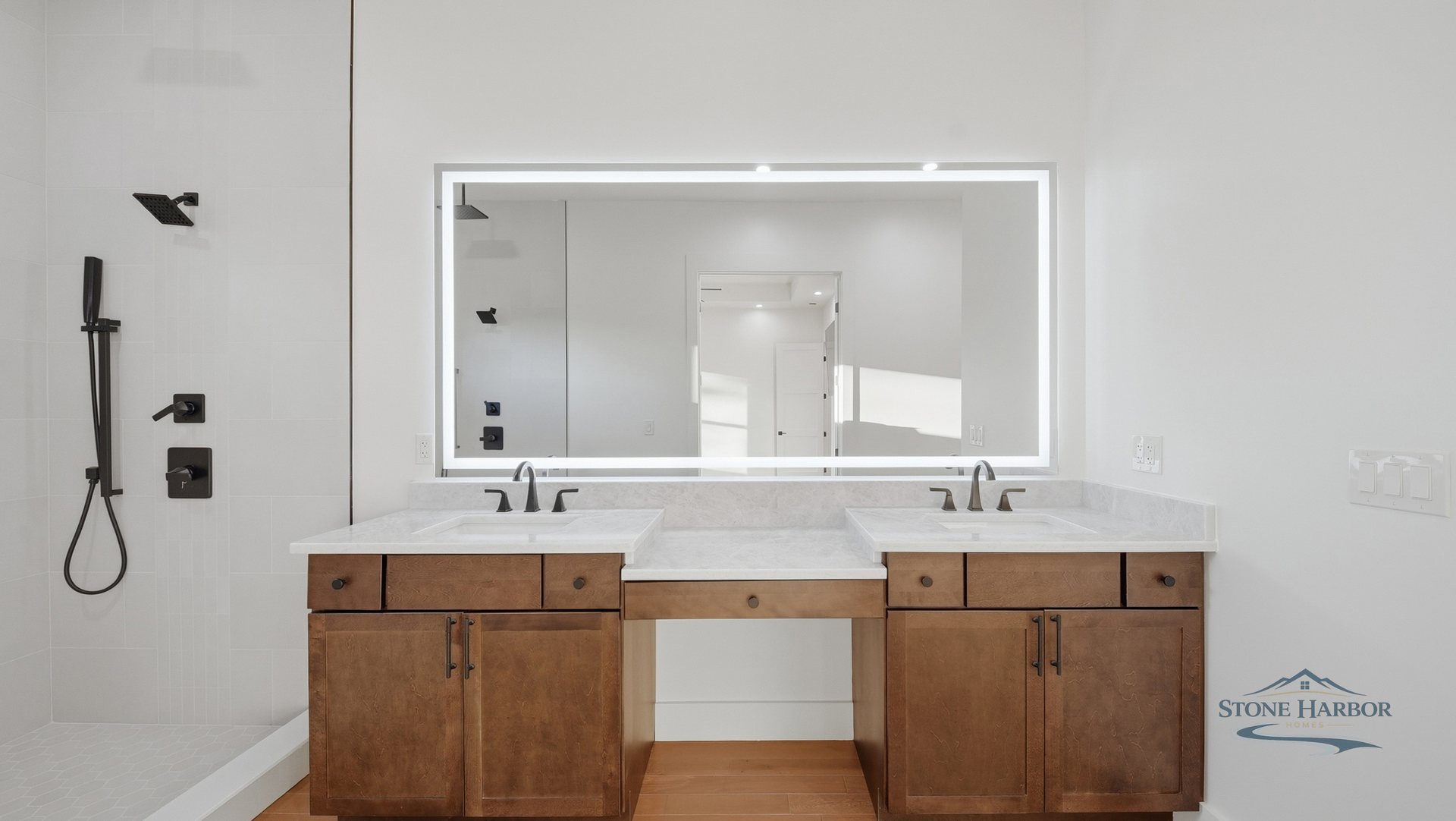 Bath with a double wood vanity, marble counters, and a tiled walk-in shower