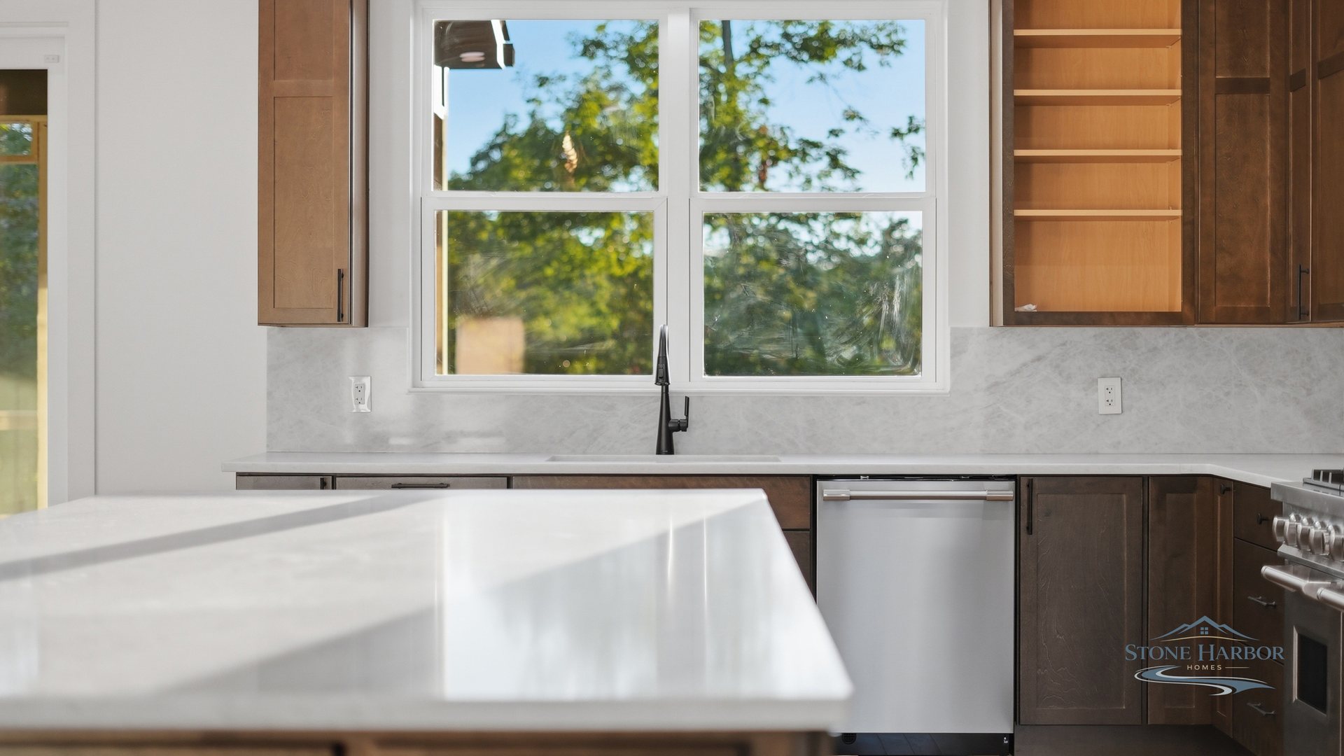 Kitchen with a waterfall-edge quartz island, stained-wood cabinetry, and a window over the counter