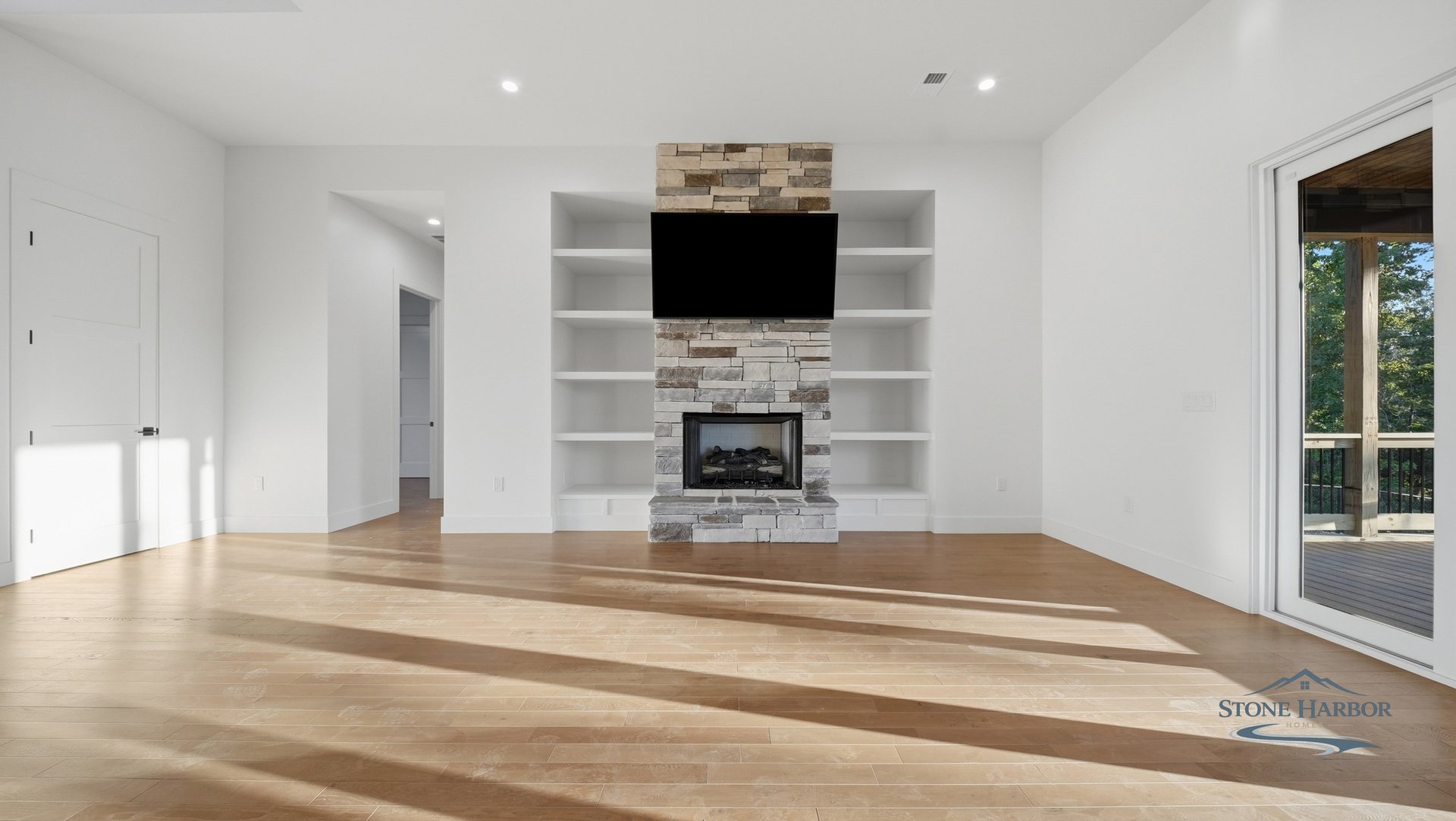 Living room with a stone fireplace, wall-mounted television, and white built-in shelving