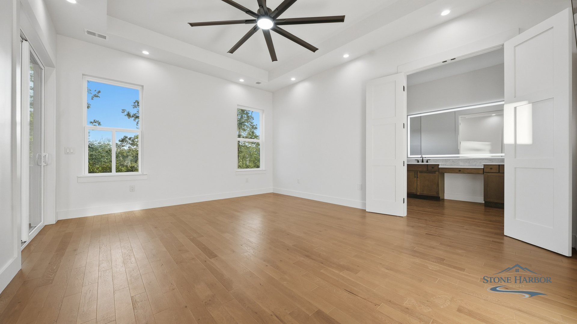 Vaulted primary bedroom with a ceiling fan and large windows