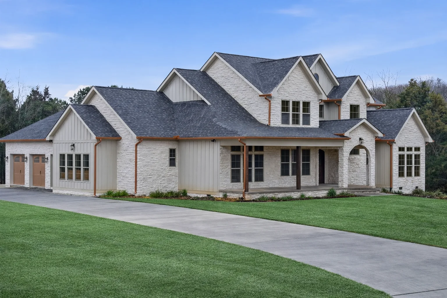 Front of a large white stone and board-and-batten home with several gables, two garage doors, and a curved concrete drive