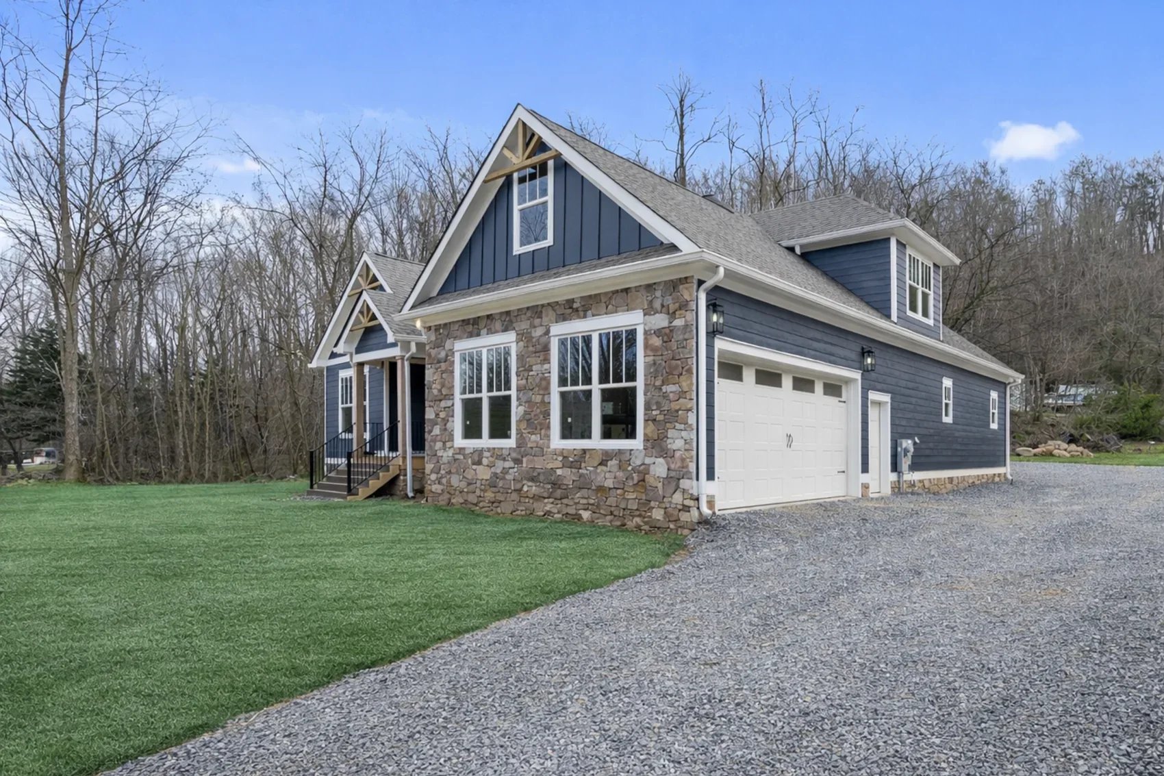 Navy blue craftsman home with a stone front, seen from its gravel driveway
